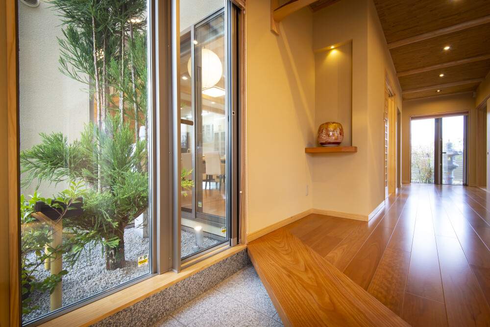 奈良の建築家が設計した数寄屋の趣を持つ和風住宅・和モダン住宅の玄関内観。土間から無垢フローリングへとつながる段差と、庭に抜ける視線設計、木の梁と間接照明による天井構成により、旅館のような落ち着きと品格を感じる空間。暮らしの質と時間の豊かさを大切にした高級注文住宅。