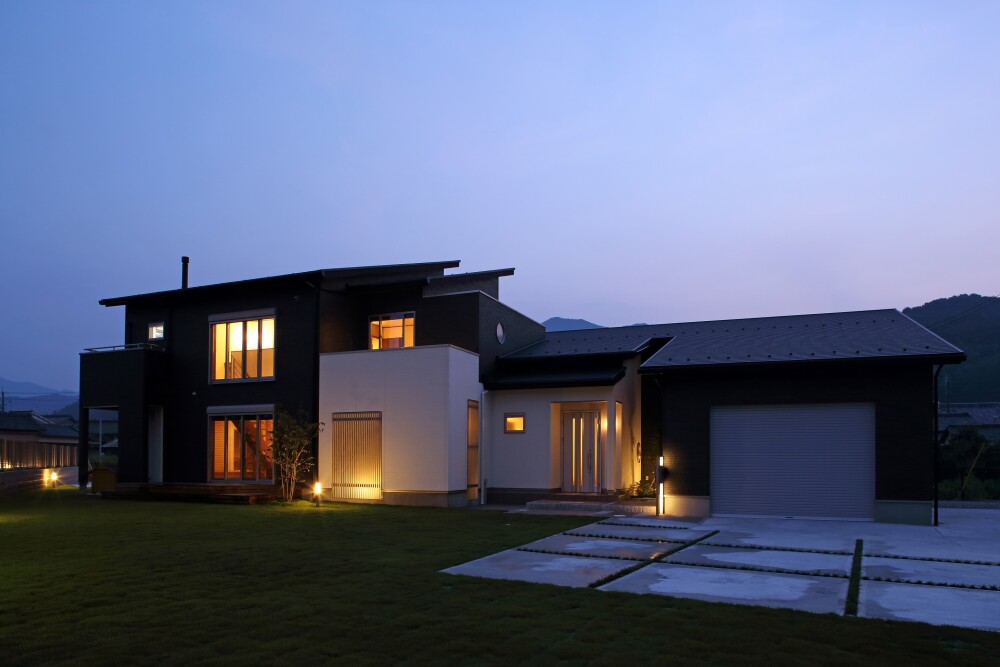 夜の静けさの中にあたたかな灯りが浮かぶ、やまぐち建築設計室による奈良県の和モダン住宅。ビルトインガレージと住空間を一体に設計した構成で、ブラックとホワイトの外壁がライトアップによって上品に際立つ。暮らしの質と美意識を両立したホテルライクな邸宅。