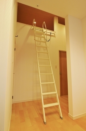 奈良の注文住宅におけるロフト付き空間の設計事例。白い可動式はしごでアクセスするロフトは、収納や書斎として活用できる多目的スペース。高天井と開放感のある室内に、木質フローリングと温かみのある照明計画を組み合わせ、和モダンとホテルライクな快適性を両立した住まい。