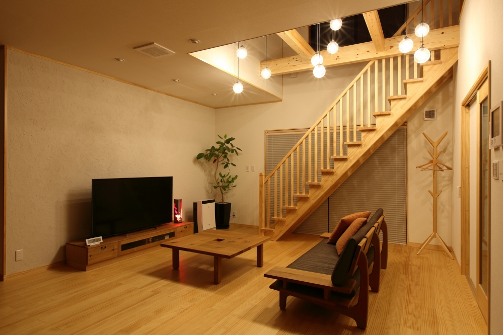 奈良の注文住宅における和モダンのリビング空間。吹き抜けとリビング階段を中心に、無垢材の床・梁・手すりを統一し、ペンダント照明を多灯配置した照明計画を採用。高天井の開放感と光の連続性により、上下階が緩やかにつながるホテルライクで上質な住まいを実現した内観デザイン事例。