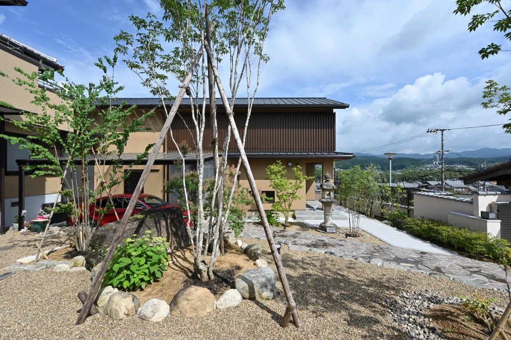 奈良県のやまぐち建築設計室が設計した和モダン住宅の外観。石と植栽で構成された庭と建築が一体となり、木格子と深い軒が陰影を生むファサード。アプローチと庭園が連続する設計により、自然と共生する静けさと上質な暮らしを実現した高級注文住宅。