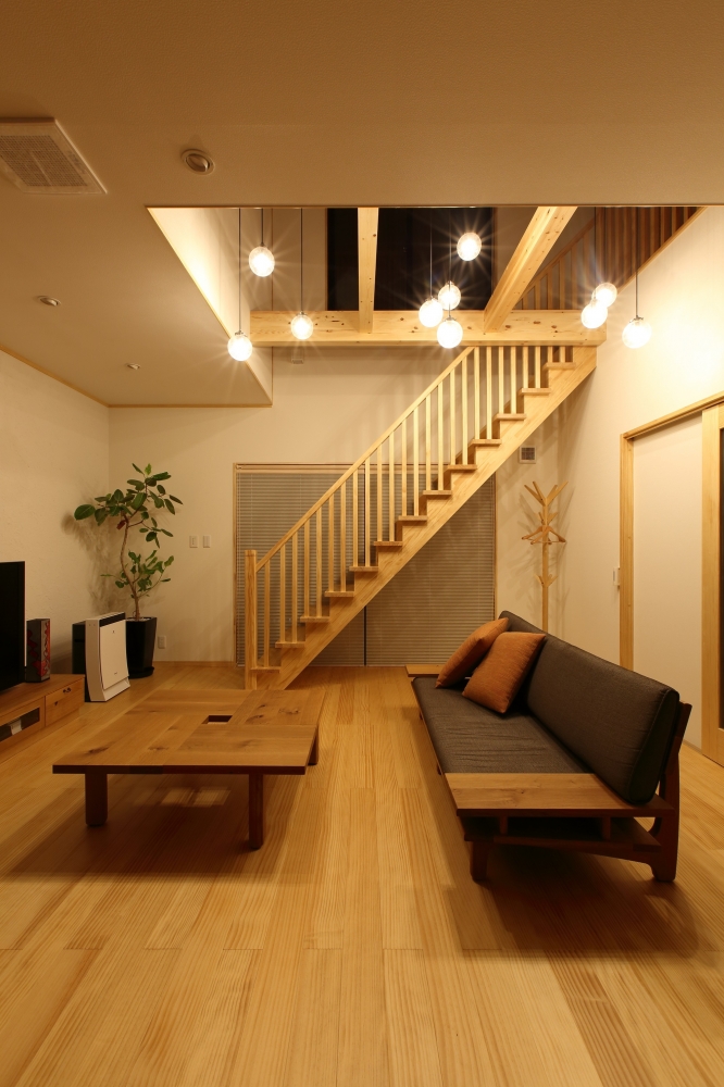 奈良の注文住宅における和モダンのリビング内観。吹き抜けとリビング階段を中心に、無垢材の床・梁・手すりを統一し、ペンダント照明を多灯配置した照明計画を採用。木の温もりと光の重なりが、ホテルライクで落ち着きのある上質な暮らしを実現する住宅デザイン事例。