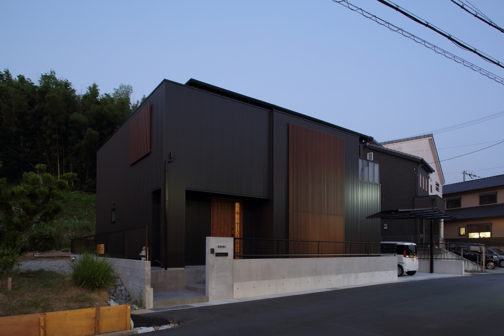 奈良の注文住宅における和モダンの外観デザイン。黒い外壁と縦格子が印象的なシンプルモダン住宅で、プライバシーを確保しながら内側に光と開放感を取り込む設計。夜景に映える外構計画と一体化したファサードが、上質で落ち着いた暮らしを演出。ホテルライクで高級感のある住まいを求める方に適した建築事例。