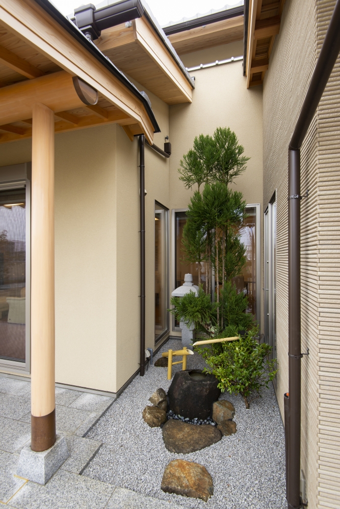 奈良県のやまぐち建築設計室が設計した数寄屋風和モダン住宅の坪庭空間。砂利敷きの中に自然石と手水鉢、竹の筧を配し、植栽とともに静けさを演出。深い軒と建物に囲まれた半外部空間が、内外を緩やかにつなぐ設計が特徴の高級注文住宅事例。和風住宅・和モダン住宅における坪庭と外構デザイン。