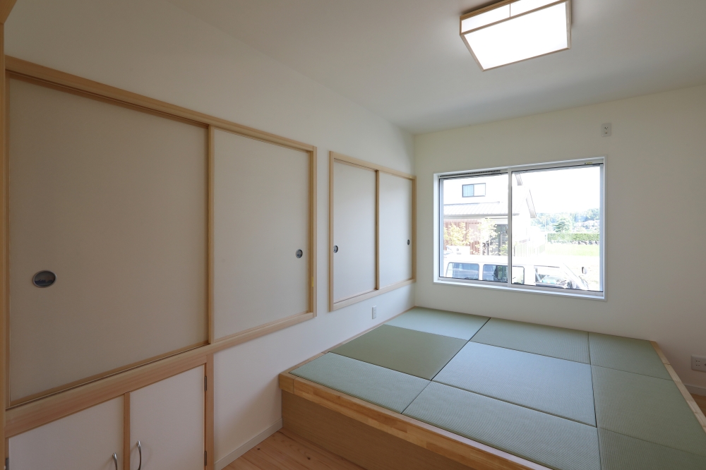 段差を活用して畳下収納を設けた、和モダン住宅の半和室空間。小上がりの畳スペースが空間に程よい区切りと落ち着きを生み出し、収納機能を兼ね備えることで、暮らしやすさと美しさを両立。白を基調とした室内に、無垢材の框や建具がやさしい温もりを添え、自然光が静かに差し込む上質な和空間を演出。注文住宅・和モダンの家・畳スペース・収納設計・自然素材の家を求める方へ向けた建築家住宅の設計事例。