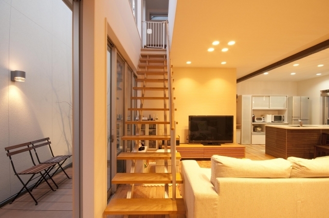 奈良の注文住宅における和モダン住宅の中間領域設計。リビング階段と屋外テラスを大開口サッシでつなぎ、内と外が連続する空間構成。無垢材の階段とデッキが視線と動線を一体化し、光と風を取り込むことで、開放感とプライバシーを両立した上質な住まいの実例。