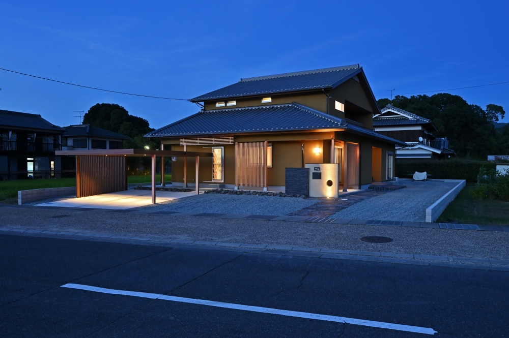 夕景に浮かび上がる、和モダンの美意識を纏った数寄屋風住宅の外観デザイン。深い軒と水平ラインを整えた黒を基調とする外観に、木格子と柔らかな間接照明が調和し、旅館のような落ち着きとホテルライクな上質感を演出。外に閉じながら内に豊かに開く設計思想により、プライバシーと開放感を両立した注文住宅。奈良県の建築家が手掛ける、和風住宅・デザイナーズ住宅・高級感のある家・都会的な和モダン住宅を求める方に向けた住まい実例。夜景の美しさ、陰影設計、外構計画、木格子、坪庭、落ち着いた照明計画など、暮らしの質を高める空間構成を丁寧にデザインした住まい。