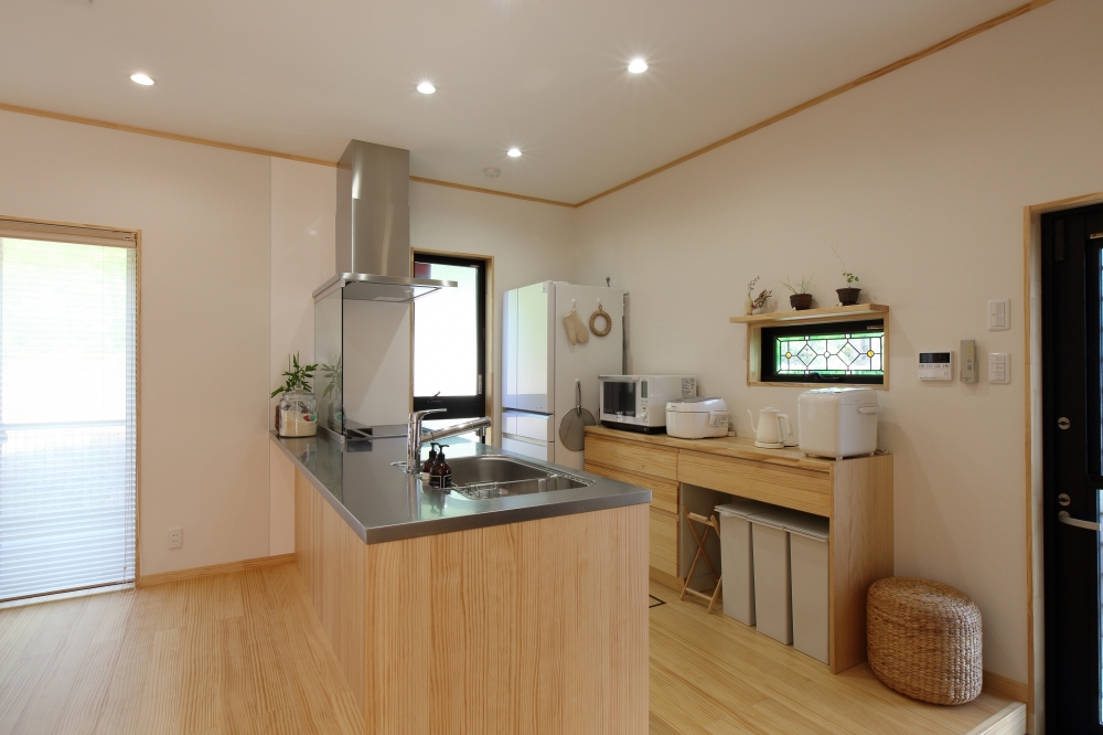 和モダン住宅の対面式キッチン空間。無垢材のカウンターとステンレス天板を組み合わせた機能的で美しいデザイン。背面には造作収納と家電スペースを整え、家事動線と収納力を両立。小窓からの自然光が空間にやわらかく広がる。奈良の注文住宅における、使いやすさと上質さを兼ね備えたホテルライクなキッチン設計事例。