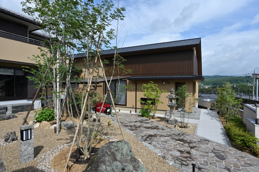 奈良県のやまぐち建築設計室が手掛けた和モダン住宅の外観。深い軒と水平ラインが美しい2階建ての邸宅に、格子デザインと自然素材を融合。石畳のアプローチと植栽、中庭的外構が調和し、ホテルライクで落ち着きのある暮らしを実現する高級注文住宅の事例。