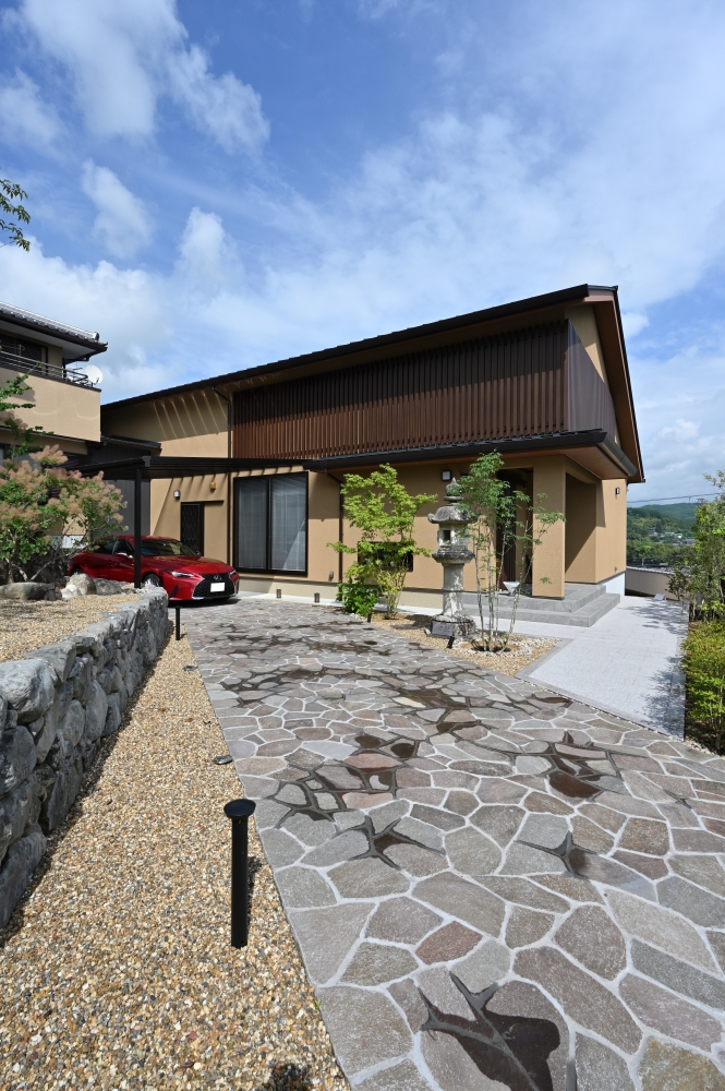 奈良県のやまぐち建築設計室が手掛けた和モダン住宅の外観。石畳のアプローチと庭園、灯籠を配した外構と、深い軒・木格子のファサードが調和し、自然と建築が連続する上質な住まい。内外の境界を曖昧にする設計で、静けさと心地よさを感じる高級注文住宅。