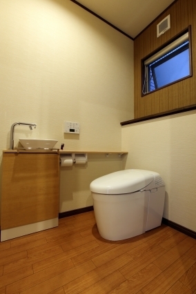 和モダン住宅のトイレ空間。木質素材と落ち着いた壁面仕上げに、コンパクトな手洗いカウンターと一体型便器を配置。高窓からの採光と通風を確保し、清潔感と静けさを両立したホテルライクな水まわり設計の事例。