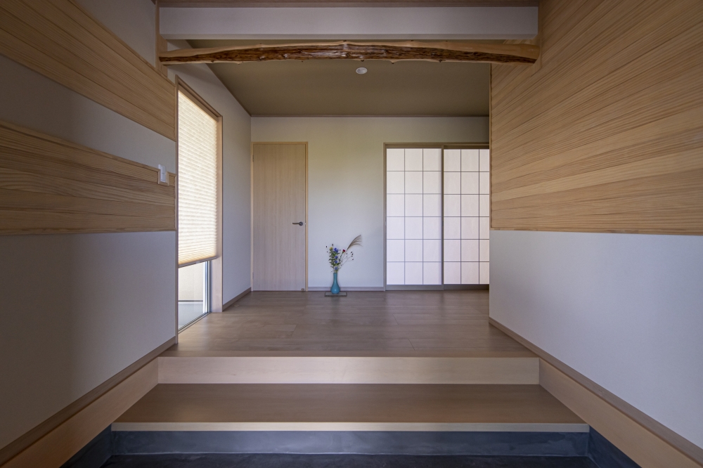 和の粋と現代的な美意識を融合した、和モダン住宅の玄関ホール空間。無垢材のやわらかな表情と左官壁の質感、床の段差構成、障子越しの穏やかな光が、旅館のような落ち着きと上質感を演出している。印象的な天然木の梁が空間に趣と個性を与え、玄関から奥へと続く視線の抜けが、静けさと広がりを感じさせる設計。和風住宅・高級注文住宅・ホテルライクな家・数寄屋風住宅・和モダンインテリア・デザイナーズ住宅を検討している方に向けた、丁寧に設計された玄関空間事例。