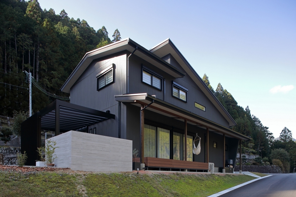 奈良の自然に囲まれた和モダン住宅の外観とアウトドアリビング空間。黒を基調としたシャープで落ち着きのあるデザインに、深い軒と水平ラインが美しく伸びる住まい。ウッドデッキと大開口の窓が内外をつなぎ、ハンモックのある半屋外空間が日常に余白とくつろぎをもたらす設計。プライバシーを確保しながら自然を取り込む、注文住宅・デザイナーズ住宅・ホテルライクな住まい。