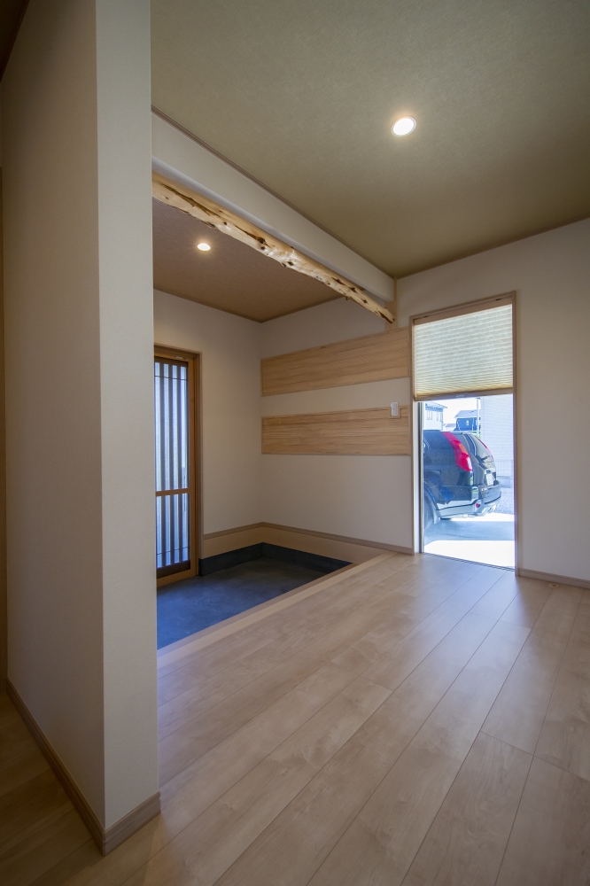 和の趣と現代的な美意識を融合した、和モダン住宅の玄関ホール空間。天然木の化粧梁とやわらかな木目、左官壁の質感が調和し、静けさと上質感を感じる設計。玄関土間からハーフビルトインガレージへ視線が抜けることで、暮らしと愛車が自然につながるホテルライクな住空間を実現している。光の入り方や空間の余白、視線の広がりを丁寧に設計し、日常に落ち着きと豊かさを与える住まい。和風住宅・和モダンの家・高級注文住宅・ビルトインガレージのある家・数寄屋風住宅・デザイナーズ住宅を検討している方に向けた建築実例。