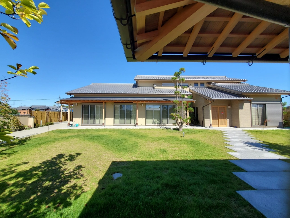 奈良県のやまぐち建築設計室が設計した和モダン住宅の庭側外観。芝生の広がる庭と一体化した開放的な設計で、深い軒と縁側空間が内外をゆるやかにつなぐ。瓦屋根と木の構造美が際立ち、自然光と陰影が心地よい住環境を生み出す高級注文住宅の事例。プライバシーと開放感を両立した奈良の邸宅。
