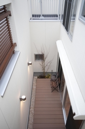 奈良の注文住宅における和モダン住宅の中庭デッキ空間。高い外壁と木製ルーバーに囲まれたプライベートテラスで、外部からの視線を遮りながら自然光と風を取り込む設計。ウッドデッキと大開口サッシが室内と連続し、開放感と安心感を両立したホテルライクな住まいの実例。