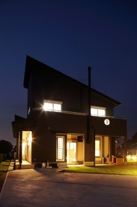 夜の静寂に包まれた和モダン住宅の外観。室内から漏れる暖かな光がファサード全体に広がり、帰宅時に安心感と落ち着きを与える設計。ダークトーンの外壁と開口部の光のコントラストが美しく、ビルトインガレージや玄関アプローチを含めた外構照明計画によりホテルライクな上質さを演出。内と外をつなぐ光の設計で暮らしの質を高めた住まい。