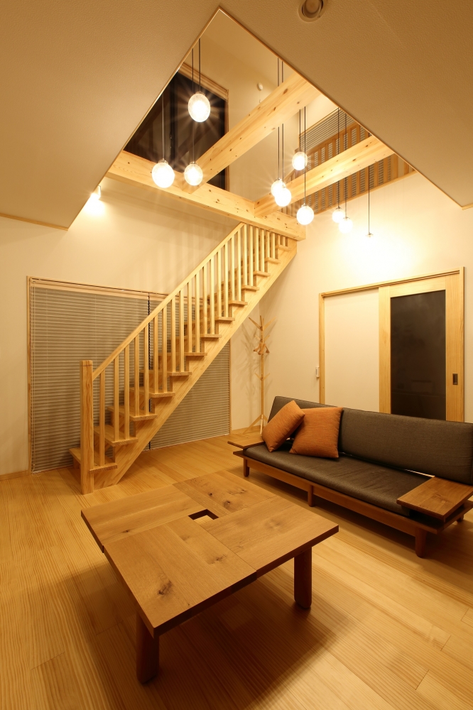 奈良の注文住宅における和モダンのリビング内観。吹き抜け空間に無垢材の梁と木製リビング階段を組み合わせ、ペンダント照明を多灯配置した照明計画により上下階の一体感を演出。木の温もりと光の重なりが、ホテルライクで上質なくつろぎを実現する住宅デザイン事例。