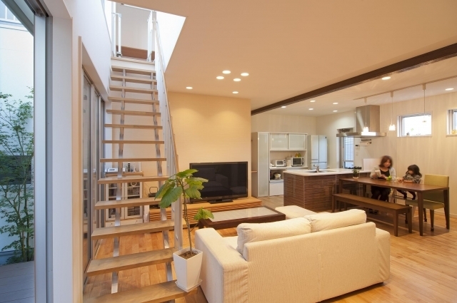 奈良の注文住宅における和モダン×ホテルライクなLDK空間。リビング・ダイニング・キッチンを一体化し、オープン階段と吹抜けから自然光を取り込みながら、中庭と連続する設計。家族の気配がつながる動線計画と家具レイアウトにより、開放感と居心地の良さを両立した上質な住まいの実例。