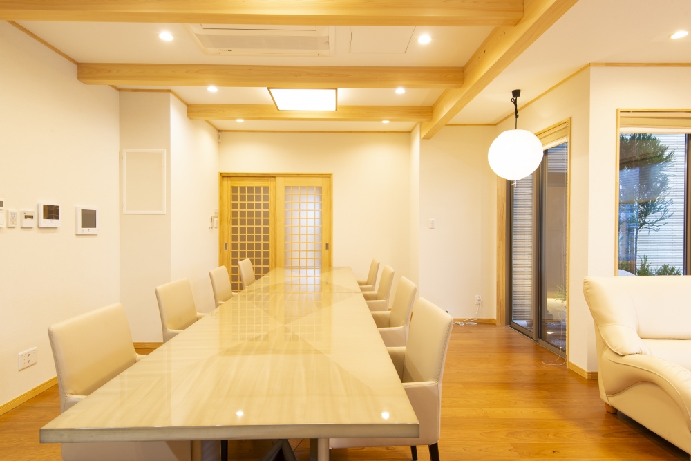 奈良県のやまぐち建築設計室が設計した和モダン住宅のダイニング空間。無垢材の梁を現した天井と長尺ダイニングテーブルを中心に据えた上質なLDK設計。障子格子の引き戸と大開口サッシにより、庭と緩やかにつながる開放的な空間構成。自然素材の温もりとホテルライクな洗練を融合し、来客対応と日常の快適性を両立した高級注文住宅の実例。