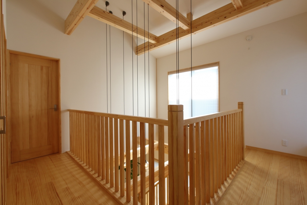 和モダン住宅の2階ホールと吹き抜け空間。無垢材の手すりと梁が美しく構成され、上階から下階へと視線と光が通り抜ける設計。ペンダント照明が空間にリズムを与え、開放感と一体感を両立。奈良の注文住宅における、上下階のつながりと居心地を大切にしたホテルライクで上質な住まいの施工事例。