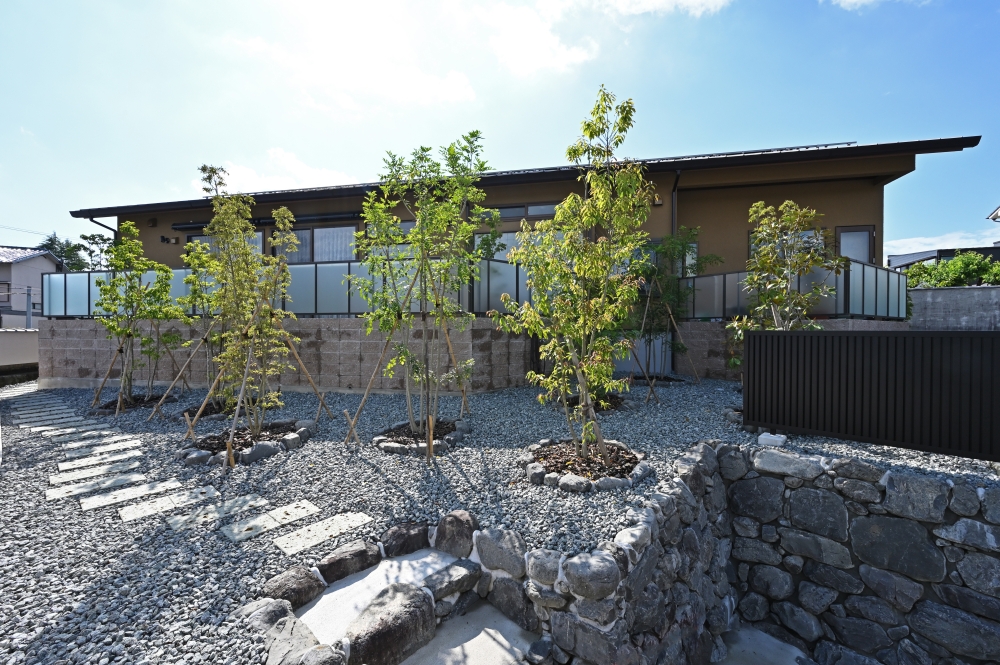 奈良県の和モダン注文住宅の外観と外構。石積みと砂利敷きの庭に植栽を配置し、建物と外構が一体となる設計。深い軒と水平ラインが美しい平屋風の住まいで、自然と調和しながら静けさと開放感を両立した住宅事例。