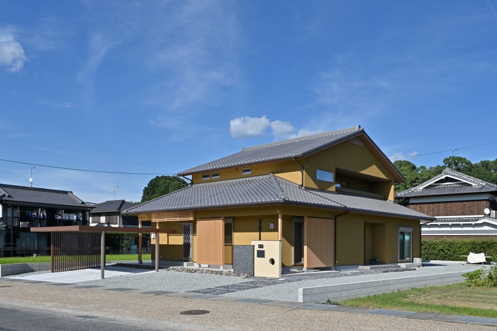 青空と自然風景に美しく調和する、和モダン住宅の外観デザイン。切妻屋根の瓦葺きと土壁調の外壁、木格子を組み合わせた数寄屋風の佇まいが、旅館のような落ち着きと上質感を演出。深い軒と水平ラインを整えた外観構成により、和の趣を大切にしながら、現代的でホテルライクな暮らしを実現した注文住宅。格子や陰影によって外からの視線をやわらかく遮り、プライバシーと開放感を両立。カーポートや外構、石張りアプローチまで建築と一体で丁寧に設計された、奈良県の建築家による和風モダン住宅実例。デザイナーズ住宅、ハイセンスな家、黒い外観の家、上質な住まいに憧れる方へ向けた建築デザイン。