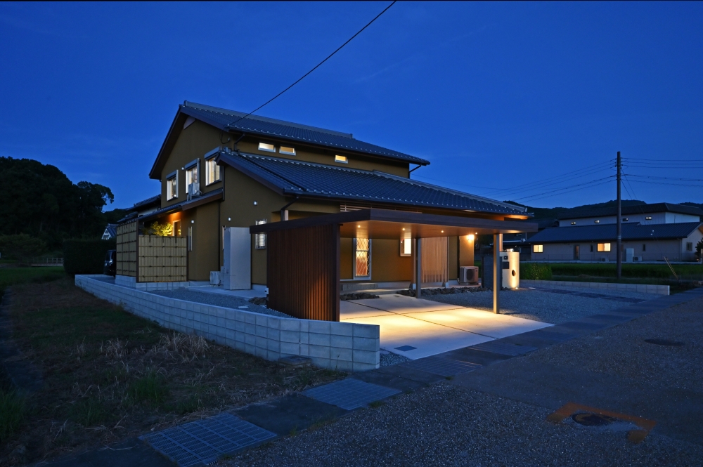 夕景の深い青空に浮かび上がる、和モダン・数寄屋住宅の外観デザイン。瓦葺きの切妻屋根と土壁調の外壁、木格子を組み合わせた上質な佇まいが、旅館のような静けさとホテルライクな心地よさを演出。水平ラインを美しく整えたカーポートや外構計画、柔らかな間接照明により、和の趣と現代的な洗練を融合した住まいを実現。外に閉じながら内に豊かに開く設計思想によって、プライバシーと開放感を両立した注文住宅。和風住宅、デザイナーズ住宅、ハイセンスな家、黒い外観の家、上質な暮らしを求める方へ向けた建築実例。夜景外観、陰影設計、木格子、車寄せ、外構デザインにこだわった和モダン住宅。