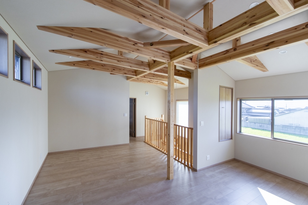 吹抜けと木組みの美しさを活かした、和モダン住宅の二階フリールーム空間。無垢材の梁を連続的に見せることで、空間全体にリズムと奥行きを生み出し、自然光がやわらかく広がる開放的な設計。二階ホールを単なる通路ではなく、読書やワークスペース、子どもの遊び場など多用途に使える“余白の空間”として計画し、暮らし方の変化にも柔軟に対応できるよう工夫している。吹抜けを介して一階LDKとつながることで、家族の気配を自然に感じられる、ホテルライクで心地よい住空間を実現。和モダンの家・吹抜けのある家・フリールーム・高級注文住宅・木の家・デザイナーズ住宅を求める方に向けた建築実例。