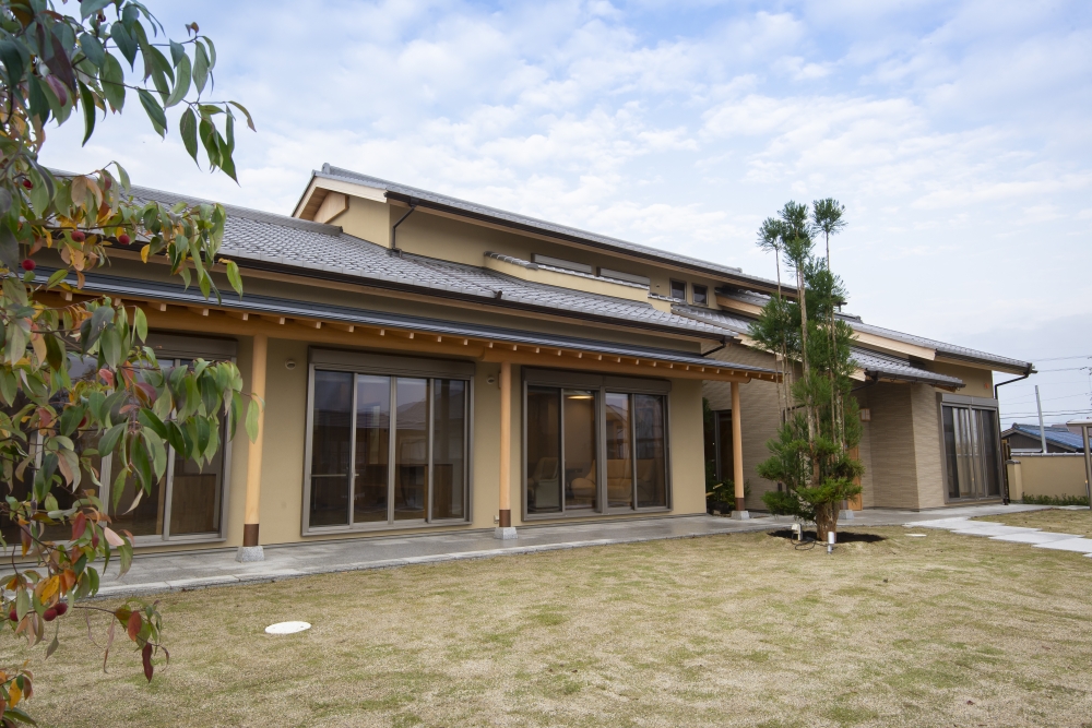奈良県のやまぐち建築設計室が設計した数寄屋風和モダン住宅の庭側外観。芝生の庭に面して連続する大開口サッシと深い軒が特徴で、室内と外部空間をゆるやかにつなぐ設計。瓦屋根と木造の柱・梁が美しい陰影を生み、植栽と建築が調和した落ち着きある高級注文住宅の事例。和風住宅・和モダン住宅の庭一体型デザイン。