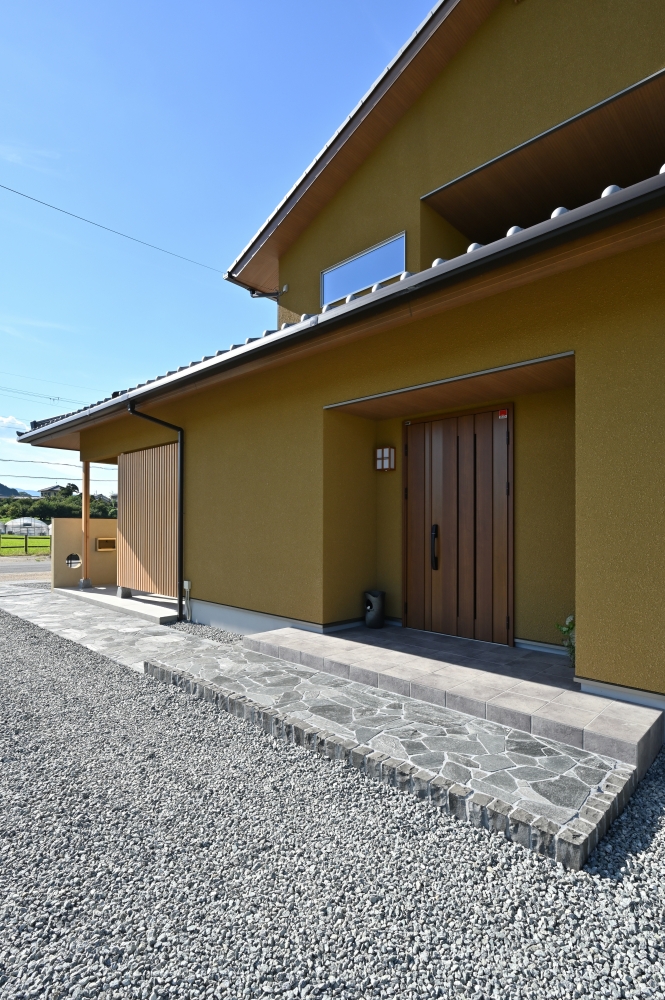 自然素材の温もりと和の美意識を丁寧に整えた、和モダン住宅の玄関外観デザイン。深い軒と木目天井、土壁調の外壁、木製玄関ドアが美しく調和し、旅館のような落ち着きとホテルライクな上質感を演出。石張りアプローチと木格子が、外からの視線をやわらかく遮りながら、住まいに奥行きと品格を与えている。奈良県の豊かな自然風景に溶け込むよう設計された、数寄屋風の和モダン住宅。和風住宅、デザイナーズ住宅、ハイセンスな注文住宅、上質な暮らしを求める方へ向けた建築実例。玄関デザイン、外構計画、木格子、陰影設計、和の素材感を大切にした住まいづくりの参考事例。