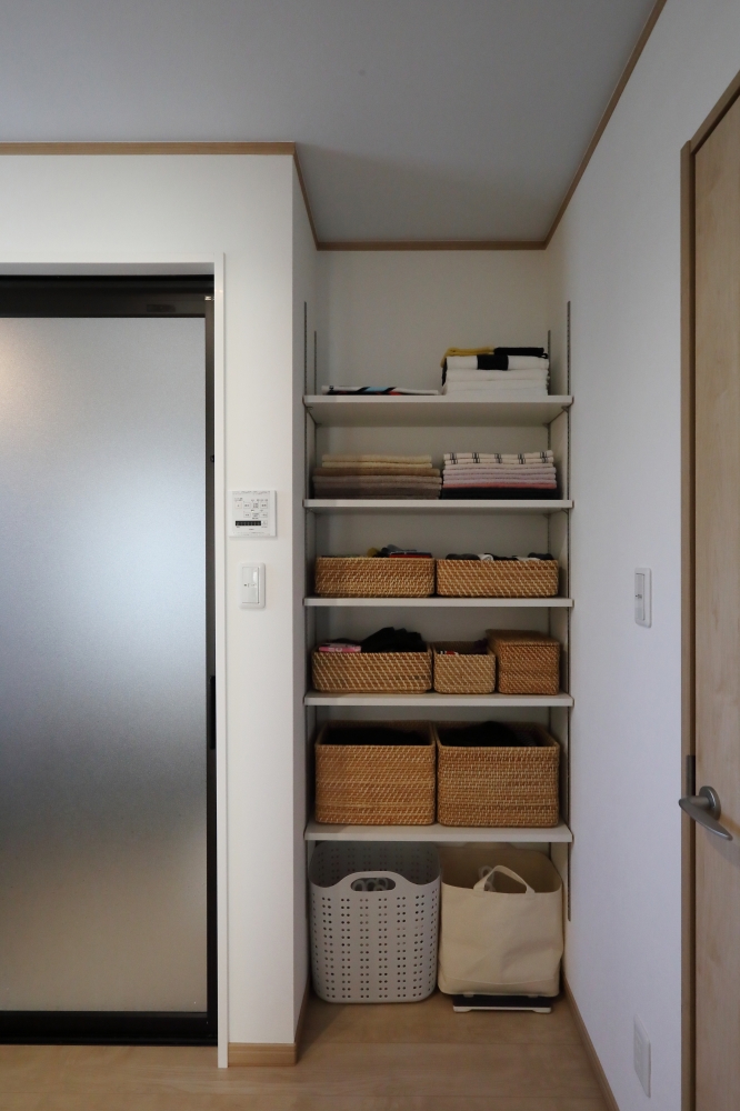 洗面脱衣室に設けた可動式収納棚が印象的な、和モダン住宅の水回り空間。タオルや日用品を美しく整理できるオープン収納を採用し、暮らしの変化に合わせて高さ調整が可能な可変性を備えた設計。生活感を抑えながらも使いやすさを重視し、家事動線と収納計画を一体的に整えることで、ホテルライクで清潔感のある空間を演出している。洗濯・収納・身支度がスムーズにつながる効率的な水回り動線により、日常の負担を軽減しながら心地よい暮らしを実現。和モダンの家・ランドリールーム・洗面脱衣室収納・家事動線・高級注文住宅・暮らしやすい間取りを求める方に向けた住宅設計事例。